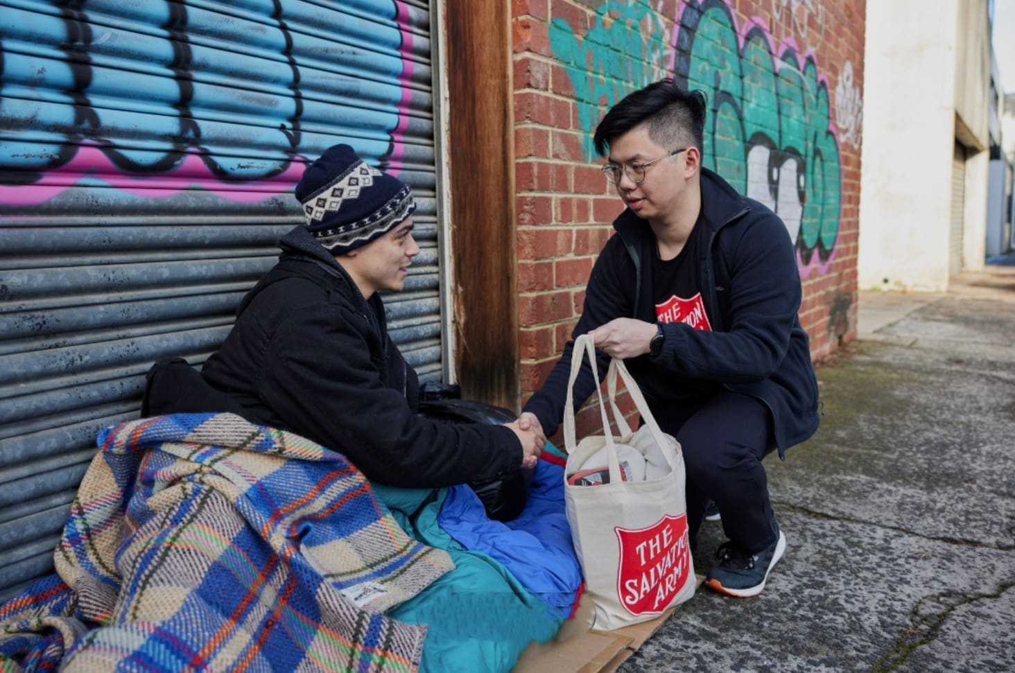 Someone handing a homeless person a bag of food and clothes.